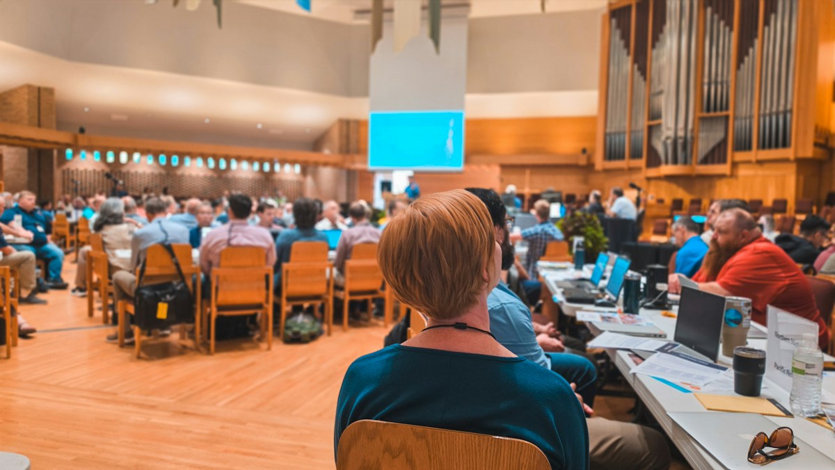 Attendees seated with laptops at a large meeting